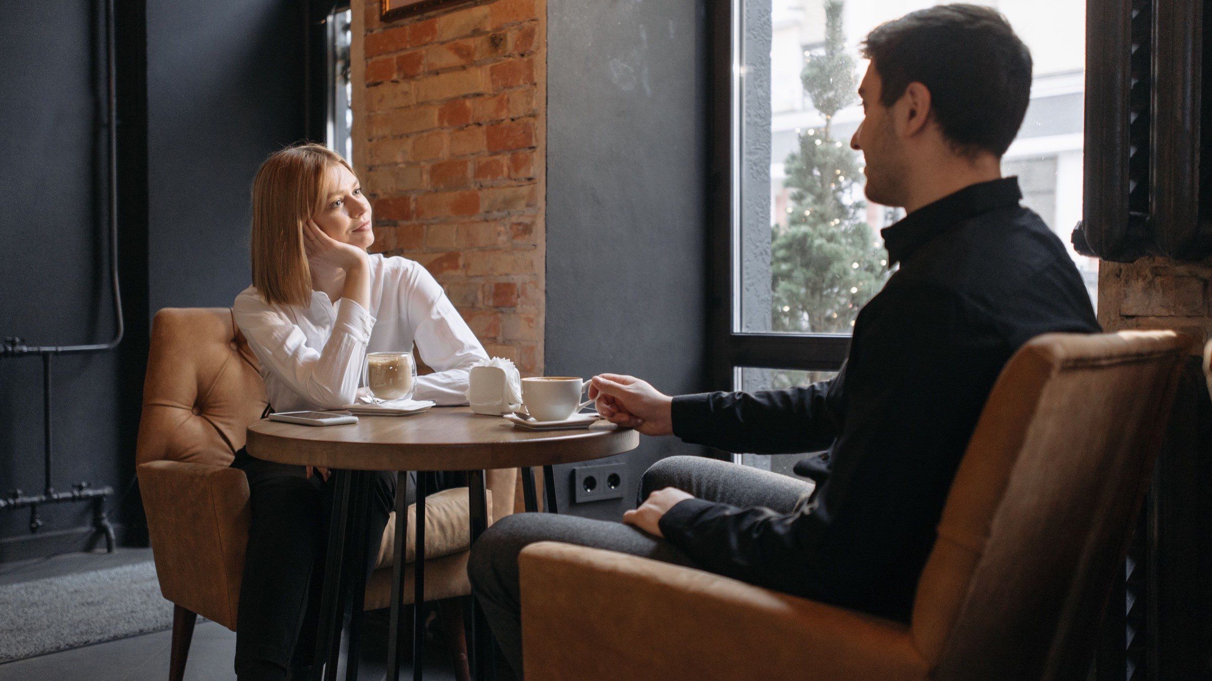 Two adults sitting across from each other at a café table with coffee, one listening attentively